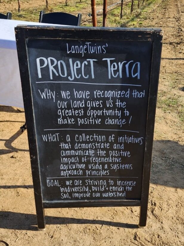 A chalkboard that reads "LangeTwins' Project Terra. Why: we have recognized that our land gives us the greatest opportunity to make positive change! What: a collection of initiatives that demonstrate and communicate the positive impact of regenerative agriculture using a systems approach principles. Goal: we are striving to increase biodiversity, build and enrich the soil, improve our watershed."