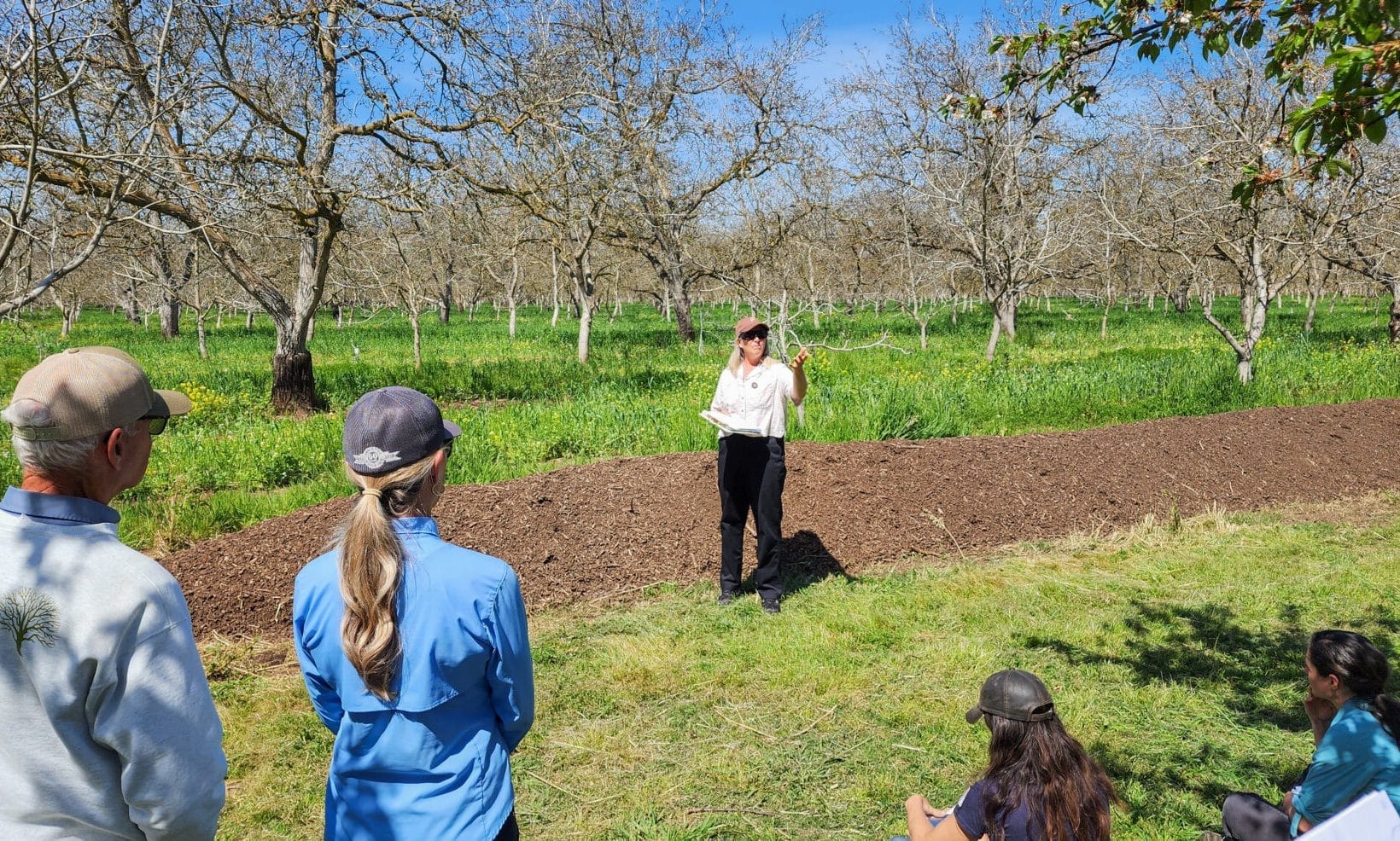 Farmers Franz and Emma speak in front of their compost, piled into a long row.